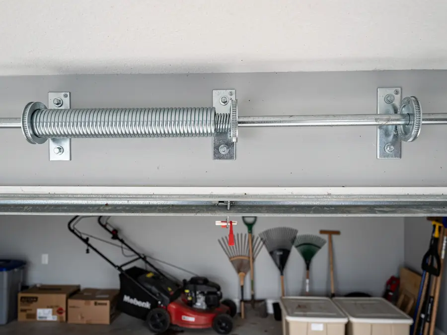 A garage door torsion spring is mounted above a garage with a lawnmower.